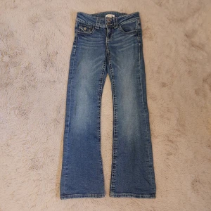 Blå bootcut jeans från Gina Tricot - Snygga blå jeans från Gina Tricot i storlek 146. Jeansen har bootcut och dubbla knappar i midjan. De har ljusa slitningar och kontrastsömmar. Perfekta för hösten och för dig dom gillarcbekväma jeans.