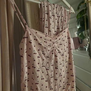 Ljusrosa pyjamas med körsbärsmönster - Ett supersöt ljusrosa pyjamassätt med tunna axelband. Trendigt från lager 157. Byxorna är i storlek XS och tröjan storlek M.