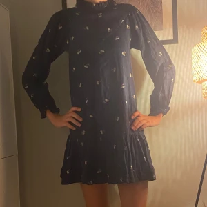 Mörkblå blommig kortklänning - Supersöt mörkblå kortklänning med små blommor, långärmad och med volang nedtill. Klänningen har en loose passform och är tillverkad i mjuk bomull. Perfekt för dig som gillar en chill och feminin stil med lite extra detaljer vid ärmslut och hals.