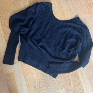 Svart omlottstickad tröja Ivyrevel - Snygg svart stickad tröja från Ivyrevel med urringad omlottdetalj baktill och bred ribbad kant nedtill. Tröjan har långärmade puffärmar och en djupare rund halsringning. 