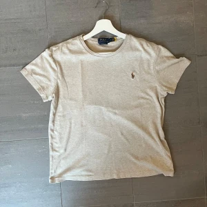 Beige t-shirt från Polo Ralph Lauren - Snygg beige t-shirt från Polo Ralph Lauren med klassisk rund hals och broderad polospelare på bröstet. Modellen är custom slim fit och har korta ärmar. Perfekt för dig som gillar stilrena och tidlösa plagg med en lyxig touch. Skicka ett meddelande vid intresse.😁
