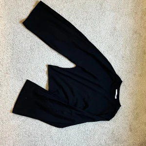 Svart långärmad tröja från 157 - En stilren svart långärmad tröja från 157, perfekt för dig som gillar enkla och cleana plagg. Tröjan har rund hals och är gjord i mjuk bomull som känns skön mot huden. Passformen är smalare i midjan och bredare upptill, liknar de virala tröjorna från nelly.  