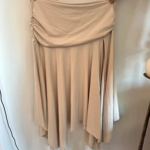 Beige långkjol med slits från SHEIN - Säljer en beige långkjol från SHEIN i storlek L. Kjolen har asymmetrisk fåll, snygg drapering i midjan och en slits på sidan. Tillverkad i mjuk polyester med lite stretch för skön passform. Perfekt för dig som gillar stilrena och trendiga plagg.
