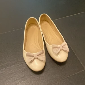 Beige ballerinaskor med rosett - Snygga beige ballerinaskor och en söt ljusbeige rosett. 