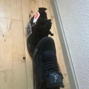 Nike Air Jordan 4 Retro Black Cat - Helt nya Säljer ett par Nike Air Jordan 4 Retro Black Cat i helsvart färg. Skorna har mesh och mockadetaljer, klassisk snörning och Jumpman-logga på plösen och sulan. Riktigt clean och tidlös siluett som passar till streetwear och sneakersamlingen.