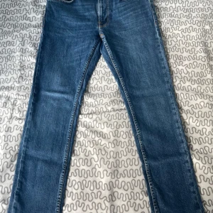 Blå jeans med raka ben - Säljer ett par klassiska blå jeans med raka ben och normal passform. Jeansen har fem fickor, snygga kontrastsömmar och är tillverkade i slitstarkt denim. Perfekta för dig som gillar en tidlös look och vill ha ett par jeans som funkar till allt.