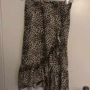 Leopardmönstrad långkjol XOXO friends - Snygg långkjol från XOXO friends med leopardmönster i beige och svart. Kjolen har volang nertill som ger en cool och trendig look. Perfekt för dig som vill sticka ut med ett djurmönster och gillar att mixa stilar.