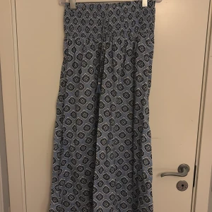 Blå långkjol från Gina Tricot - Supersnygg långkjol från Gina Tricot i blått med vitt och mörkblått blommönster. Kjolen har smock i midjan för en bekväm passform och är gjord i ett lätt och luftigt material. Perfekt för dig som gillar boho-vibbar och vill ha något flowy till sommaren.