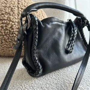 Svart handväska Massimo Dutti - Svart axelväska med flätade detaljer längs sidorna och ett stilrent handtag. Väskan har mindre slitage (se bild) annars sparsamt använd. Köpt på Massimo Dutti. 