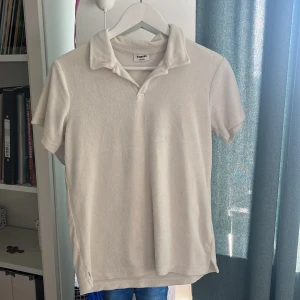 Vit frotté t-shirt från Kappahl - Snygg vit t-shirt från Kappahl i mjuk frotté. Modellen har korta ärmar, klassisk krage och v-ringad hals. Perfekt för en chill och avslappnad stil. Passar dig som gillar bekväma och stilrena plagg.