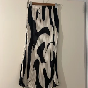 Plisserad svartvit långkjol - Säljer en plisserad långkjol med coolt svartvitt mönster som påminner om zebra. Kjolen har elastisk midja och är gjord i mjuk polyester med lite stretch. Perfekt för dig som gillar statement-plagg och vill sticka ut med en unik look.