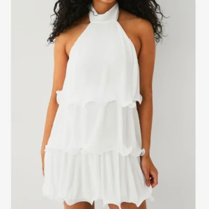 Vit klänning med volanger - Supersöt vit kortklänning med halterneck och knyt i nacken. Klänningen har flera lager med volanger som ger en flowy och luftig känsla. Perfekt för sommarens alla tillfällen. Aldrig använd!😍Skriv för fler bilder