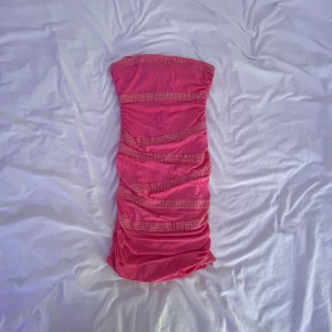 Rosa tubklänning med paljettdetaljer - Snygg rosa kort tubklänning från I AM VELVET med glittriga paljettdetaljer i rader framtill. Klänningen är tight och ärmlös, perfekt för dig som vill sticka ut. Materialet är mjukt och stretchigt, vilket gör den bekväm att bära hela kvällen.