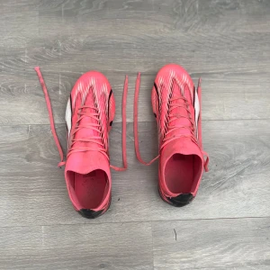 Puma rosa fotbollsskor med snörning  - Säljer ett par grymma puma fotbollsskor i stark rosa med svarta och vita detaljer. Skorna har snörning, platt sula med dobbar och ett snyggt grafiskt mönster på ovansidan. Perfekt för dig som vill sticka ut på planen och ha maxad kontroll på bollen.
