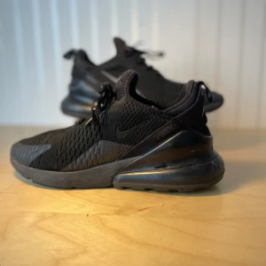 Svarta Nike Air Max 270 sneakers - Nike Air Max 270 sneakers i helsvart färg med mesh-överdel och synlig Air-enhet i hälen. Snygg sportig design med snörning och rund tå. Perfekt för dig som gillar streetstyle och vill ha bekväma skor med grym dämpning. Storlek EU 42.5, US 8.5.