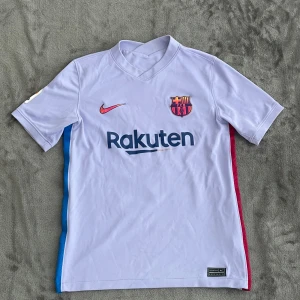 Barcelona Pedri 16 fotbollströja Nike - Snygg Barcelona fotbollströja med Pedri 16 på ryggen, tillverkad av lätt polyester. Tröjan är ljuslila med röda och blå detaljer på sidorna, har klubbmärke på bröstet och Rakuten-logga. Kortärmad med La Liga-märke på ärmen och klassisk krage. Köpt i Shoppen på camp nou (barcelonas arena) så den är 100% äkta