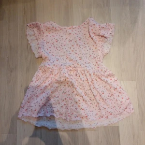 Ljusrosa blommig blus Lindex - Supersöt ljusrosa blus från Lindex med små blommor på. Blusen har volangärmar och en liten rosett i midjan. Aldrig använd. Storlek 158-164 men passar storlek XS eller S i vuxenstorlek.  