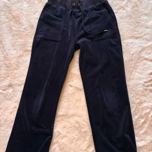 Mörkblå velourbyxor Juicy Couture XS - Mörkblå mjukisbyxor från Juicy Couture i velour med bred resårmidja och snörning. Byxorna har stora fickor fram, bakficka med knappar och broderad JC-logga. Perfekta för en chill och trendig look. Byxorna är köpta på damavdelning.