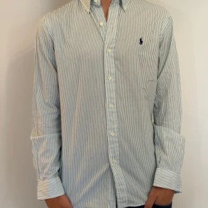 Randig skjorta från Ralph Lauren S - Snygg vit skjorta med smala gröna ränder från Ralph Lauren. Slim fit-modell med klassisk krage, knappar framtill och broderad logga på bröstet. Långärmad och tillverkad i mjuk bomull. Perfekt för dig som gillar stilrena och tidlösa plagg.