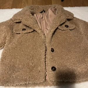 Beige teddyjacka med stora knappar - Säljer en beige teddyjacka med fluffigt material och bred krage. Jackan har två framfickor med lock och stora mörka knappar framtill. Perfekt för dig som gillar mysiga och trendiga jackor med lite oversized känsla.