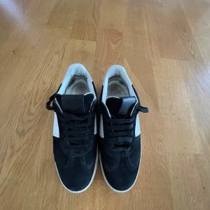 Valentino flycrew sneakers svart/vit - Säljer ett par Valentino flycrew sneakers i svart och vitt skinn med mockadetaljer. Snygg camouflagemönstrad sula och klassisk snörning. Perfekt för dig som gillar exklusiva och stilrena sneakers med coola detaljer. Några spikar på skorna har ramlat av.