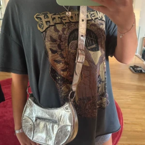 Silvrig axelväska i skinn - Säljer en snygg silvrig axelväska i skinn med justerbart axelband och coola metalldetaljer 