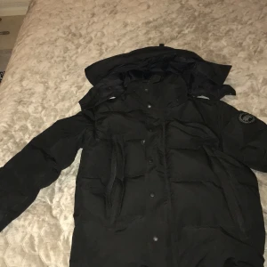 Canada goose wyndham jacka (Size M) - Säljer en svart dunjacka från Canada Goose i storlek M. Jackan har huva, dragkedja och knappar framtill samt logga på ärmen. Perfekt för kalla dagar med sin tjocka och fluffiga känsla. Snygg och stilren design som håller dig varm hela vintern. 3600kr vid snabb köp annars kan vi snacka och ta ner priset. Jackan är helt äkta fast när jag köpte den så var den för stor och då har jag redan tagit på mig den och canada goose ville inte ha den tillbaka 