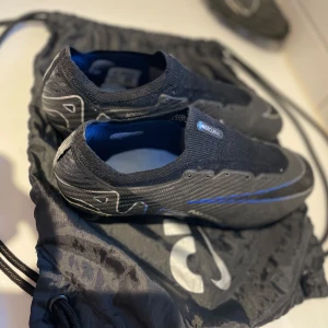 Nike Mercurial Zoom fotbollsskor svart/blå - Säljer dessa grymma fotbollsskor som verkligen är bland de bästa jag någonsin har spelat i. Tyvärr passar de mig inte längre, annars hade jag aldrig gjort mig av med dem. Skorna är i bra skick,inga skador på skon över huvudtaget. Dobbarna är fortfarande i helt okej skick och de håller garanterat för många matcher till. Det enda problemet är att skorna saknar sina snören. Skornas Nike  påse följer självklart med på köpet. Perfekt för dig som vill ha ett par bra skor till ett bra pris!