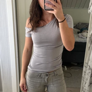 Ljusgrå offshoulder topp - Säljer en ljusgrå, tight offshoulder topp med kort ärm. Toppen har en asymmetrisk axel och sitter figurnära med rynkade sidor. Perfekt för dig som gillar en enkel men snygg stil. Materialet känns mjukt och stretchigt. Från Gina, storlek S. Knappt använd. 