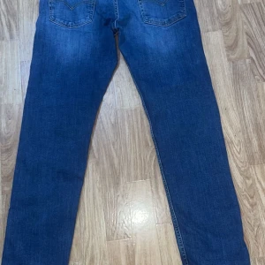 Levi's 502 blå jeans W31 L30 - Säljer ett par klassiska Levi's 502 jeans i snygg blå färg. Modellen har rak passform och normal midja, med fem fickor och tydliga sömmar. Materialet är slitstarkt jeans och de har den ikoniska Levi's-lappen bak. Perfekt för dig som gillar tidlös stil.
