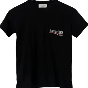 Svart Balenciaga t-shirt med tryck - Svart t-shirt från Balenciaga med vit och röd logga tryckt både fram och bak. Klassisk rund hals och korta ärmar. Materialet är mjuk bomull som känns skönt mot huden. Snygg och enkel design med cool branding för dig som gillar streetwear.