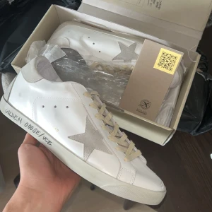 Golden Goose Grå med design - Golden Goose grå mockastjärna på sidan och beige snörning. Handskriven text på sulan. Kommer med originalkartong och dustbag. Finns en del märken på att de använts. Skick 7/10 Pris ej ristat i sten