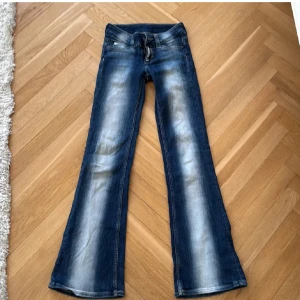 Blå bootcut jeans med slitningar - Snygga blå jeans med bootcut-modell och slitna detaljer framtill. Jeansen har klassisk femficksdesign, dragkedja och knapp i midjan. Perfekta för dig som gillar en retro vibe och vill ha ett par jeans med lite extra attityd.