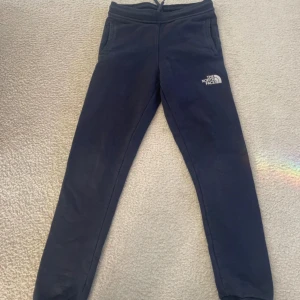 Mörkblå mjukisbyxor The North Face - Barn 13 år - Mörkblå mjukisbyxor från The North Face med logga på låret. Byxorna har resår i midjan med snörning och två sidofickor. Tillverkade i mjuk bomull, perfekta för chill eller träning. Snygg och enkel design som funkar till det mesta.