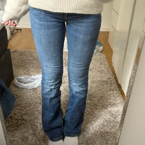 Blå bootcut jeans låg midja - Snygga blå jeans med bootcut och låg midja. Klassisk femficksmodell med smal passform upptill och utsvängda ben. Jeansen är i ett mjukt denimtyg och har detaljerade sömmar och bälteshällor. Perfekta för en avslappnad och trendig look.