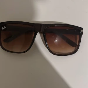 Ray-Ban bruna fyrkantiga solglasögon - Snygga solglasögon från Ray-Ban med fyrkantig form och bruna bågar. Glasen är tonade i brunt och ger en cool vibe. Perfekta för att lyfta din stil under soliga dagar. Klassisk Ray-Ban-logo i hörnet på linsen. De är inte riktiga dm om ni har ett prisförslag 