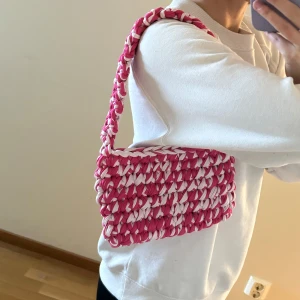 Hemmavirkad väska i rosa/vit  - Hemmavirkad handväska, gjord i t-shirtgarn som är gjort av textilindustrins tygöverskott.   Mått: ca 22cm bred, 15cm hög och 38cm hög (inklusive handtag)