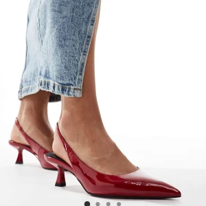 Röda pumps med spetsig tå - Helt nya Snygga röda pumps med glansig finish och spetsig tå. Skorna har en låg klack och öppen häl med smal rem runt foten. Köpte fel storlek.