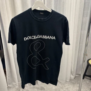 Svart Dolce & Gabbana t-shirt - Svart t-shirt från Dolce & Gabbana med stort vitt logotryck och ampersand på framsidan. Klassisk rund halsringning och korta ärmar. 
