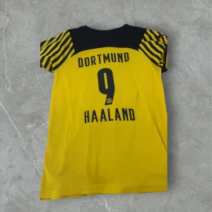 Borussia Dortmund puma tröja - Gul och svart Borussia Dortmund matchtröja med Haaland och nummer 9 på ryggen. Klassisk design med svarta ränder på ärmarna, klubbmärke och Puma-logga framtill. Tillverkad i lätt och ventilerande material, perfekt för fotbollsfans.