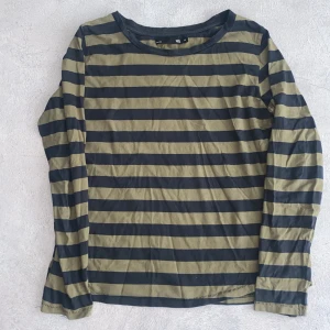 Randig långärmad tröja 157 M - Randig långärmad tröja från 157 i svart och olivgrön. Klassisk rund halsringning och raka ärmar. Tillverkad i mjuk bomull, perfekt för en chill och avslappnad stil. Passar dig som gillar basic men ändå vill sticka ut lite med mönster.