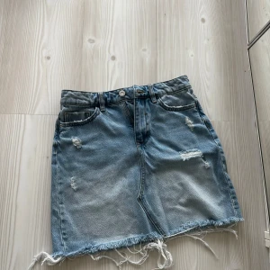 Blå jeanskjol med fransad kant från Zara - Säljer en snygg blå jeanskjol från Zara i storlek XS. Kjolen har fransad kant nedtill, slitna detaljer och klassiska fickor både fram och bak. Perfekt för dig som gillar en chill och trendig stil.