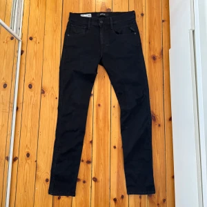  Replay Anbass Hyperflex Jeans - Säljer ett par svarta jeans från Replay, modell Anbass hyperflex, storlek W31 L32. Klassisk femficksdesign, snygga detaljer och diskret Replay-logga vid fickan. Jeansen är tillverkade i stretchigt material för en bekväm passform.