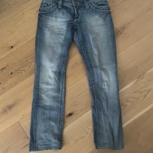 Blå bootcut jeans med dragkedjor - Säljer ett par blå bootcut jeans från indian rose med snygga slitningar och dragkedjor på bakfickorna. Jeansen har låg midja och klassisk femficksdesign. Perfekta för dig som gillar en avslappnad men ändå trendig look. Midjemått 36 cm 88 cm långa. Har sytt in dom lite. 