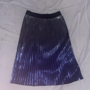Glittrig plisserad kjol från Lindex - Snygg plisserad kjol från Lindex i metallic silver och lila. Kjolen har glittrig finish och bred resår i midjan för extra komfort. Perfekt för dig som vill sticka ut med en cool och trendig look.