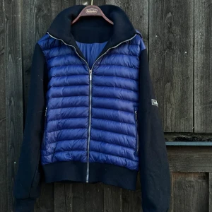 Blå cardigan från Levon - Snygg blå cardigan från Levon med svarta ärmar och krage. Cardigan har quiltad front i glansigt material, dragkedja hela vägen och ribbade muddar. Perfekt för dig som vill vara grisch. En luva finns också som man kan sätta på och av. Den passar även storlek M. Kan gå ner lite i pris vid snabb affär. Nästan aldrig använd skicket är 9/10 nästan nyskick, skriv DM vid förderingar eller intresse. 