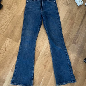Blå bootcut jeans från Gina Tricot - Snygga blå bootcut jeans från Gina Tricot, modell Perfect Jeans. Klassisk femficksdesign, hög midja och utsvängda ben. Jeansen är i ett mjukt denimtyg som sitter skönt och ger en tidlös look. Perfekta för dig som gillar retrovibbar och vill ha en cool siluett.