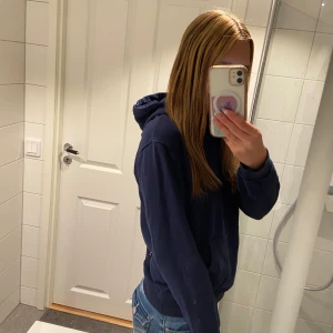 Mörkblå hoodie med huva - Säljer en enkel och snygg mörkblå hoodie med huva och stor magficka. Tröjan har lång ärm och en loose passform som är perfekt för chill dagar. Materialet är väldigt mjukt och skönt. Och den är lite för liten för mig så därför ser den liten ut på bilden.