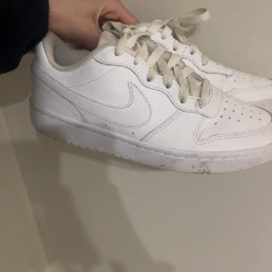 Vita Nike sneakers - Säljer ett par klassiska vita Nike sneakers med snörning och rund tå. Skorna har en stilren design med vit sula och ovandel i syntetmaterial. Perfekta för en clean och sportig look.