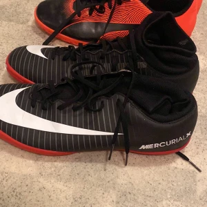 Nike  fotbollsskor  - Säljer ett par Nike Mercurial fotbollsskor med högt skaft. Skorna är svarta med vita och röda detaljer samt har snörning och en stor vit Nike-logga på sidan. Perfekta för dig som vill ha bra grepp och stil på planen. I bilden finns det två lar skor och båda har storlek 41 säljer en för 150kr eller två för 250kr